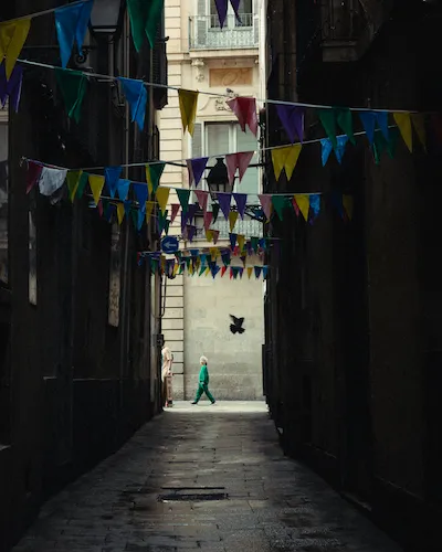 A narrow alleyway in Barcelona, a young boy in a green outfit walking through the center.